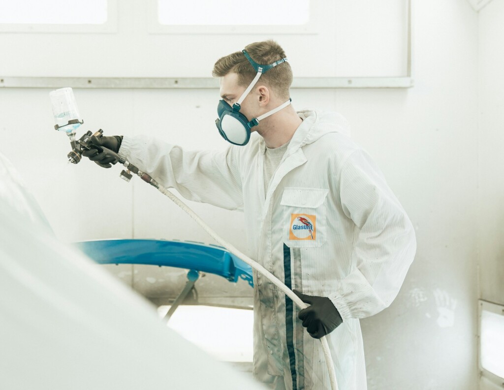 A professional in protective gear spray paints a car in a workshop.