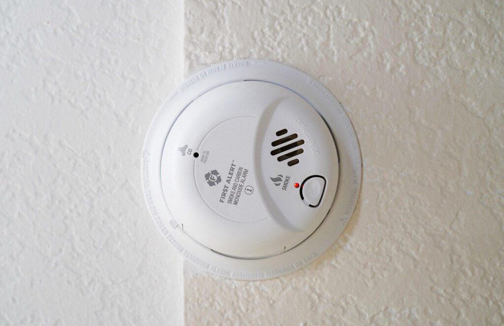 A smoke and carbon monoxide alarm mounted on a textured white wall.