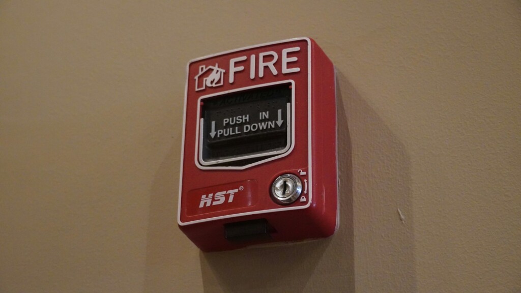 A red fire alarm pull station mounted on a beige wall.