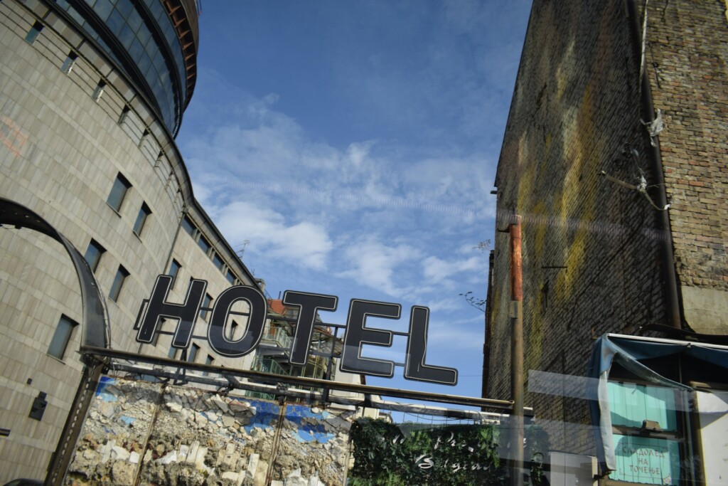 A large "HOTEL" sign against a backdrop of urban buildings and blue sky.