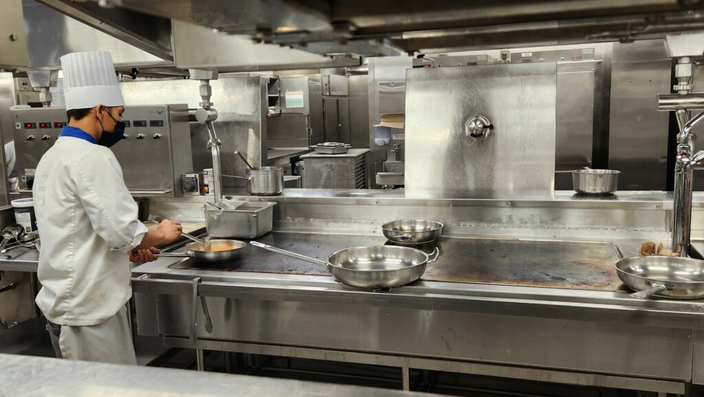 A chef in a white uniform cooks in a professional stainless steel kitchen.