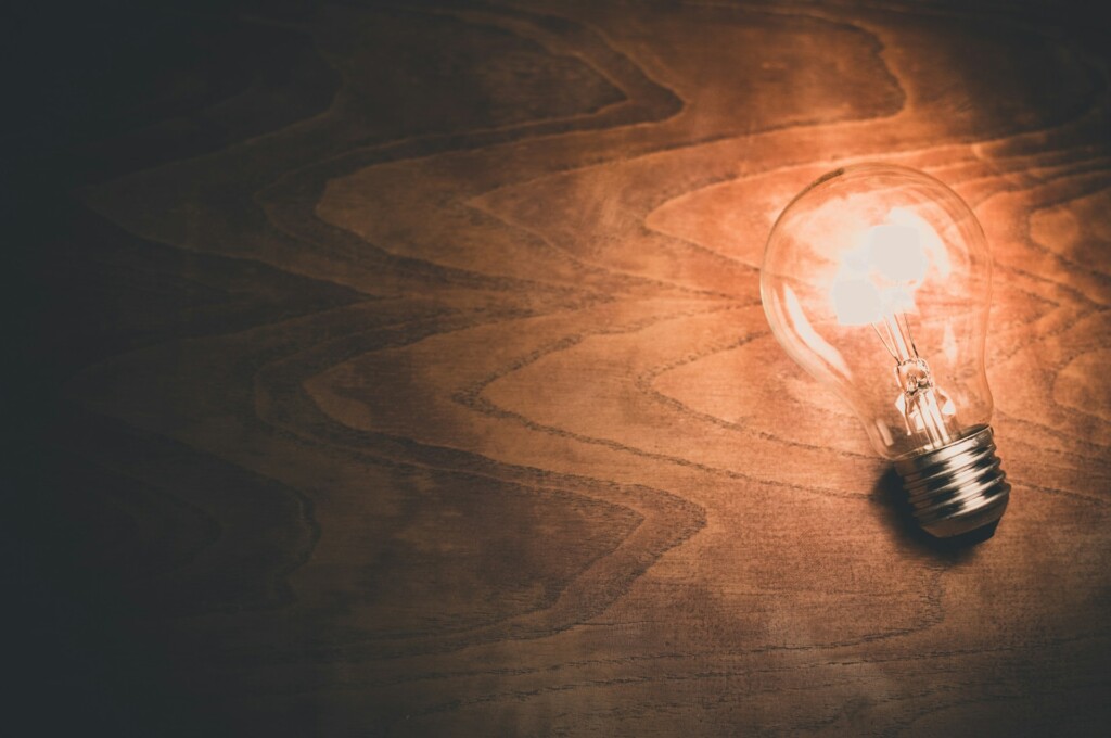 A glowing light bulb lies on a wooden surface with warm lighting.