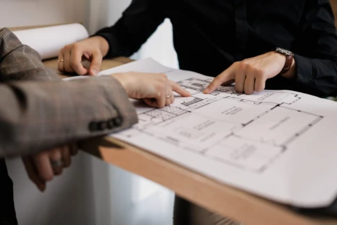 Two people discussing a floor plan at a wooden table.