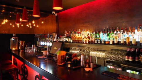 A dimly lit bar with colorful bottles and red pendant lights.