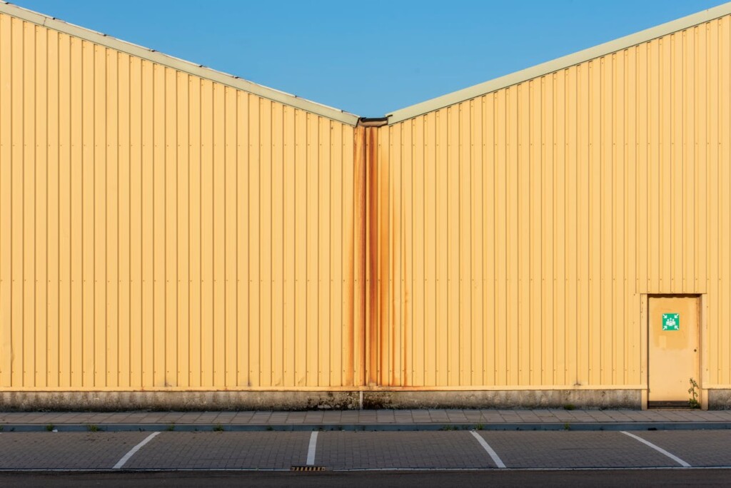 Yellow industrial building facade with rust streaks and a small door.