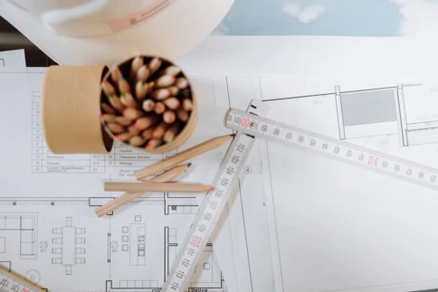 Architectural blueprint with colored pencils and a measuring tape on top.