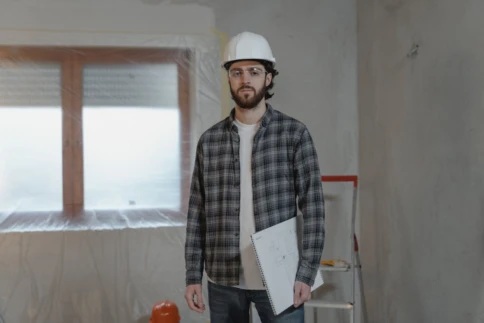 Man wearing a hard hat holds architectural drawings in a construction site.