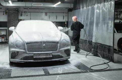 Car partially covered in soap being washed by a person in a garage.