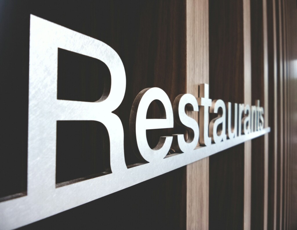 White 3D "Restaurants" sign on a wooden wall in close-up view.