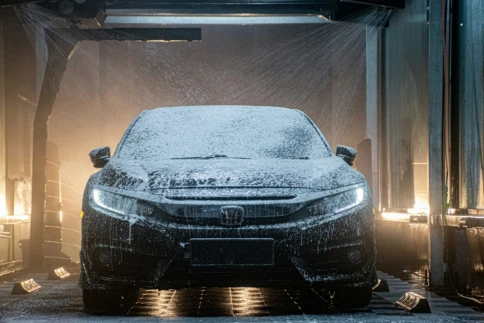 A car covered in soap is being washed in an automatic car wash.
