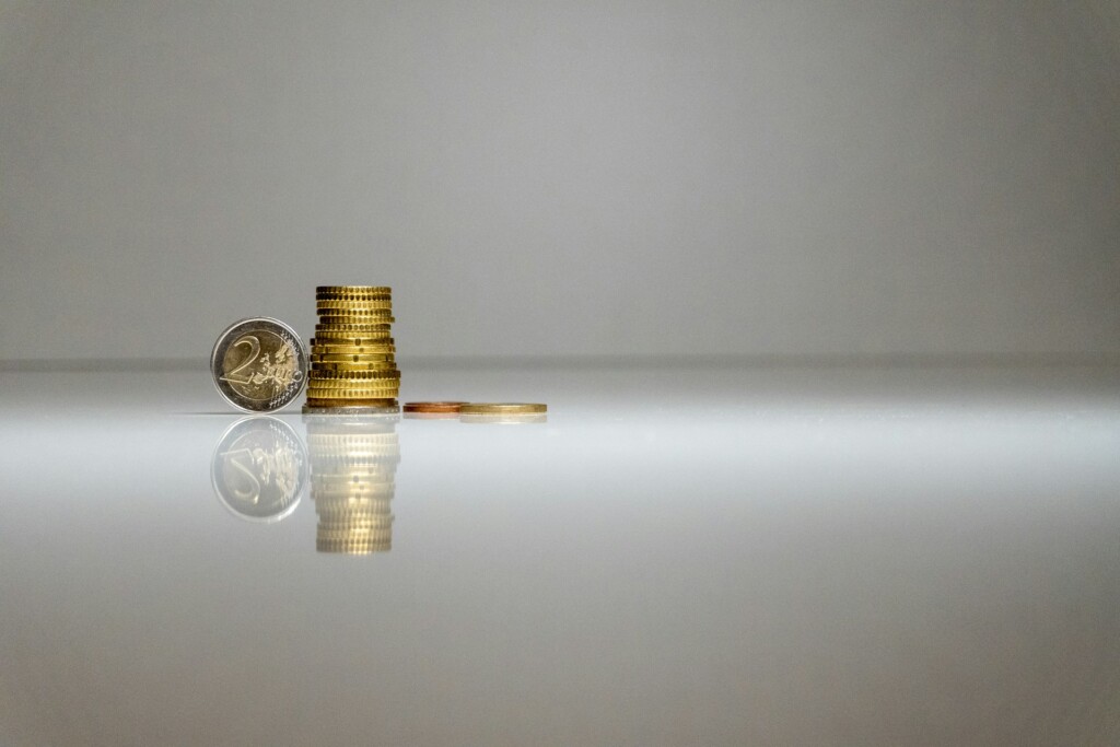 A stack of coins and a single coin on a reflective surface.