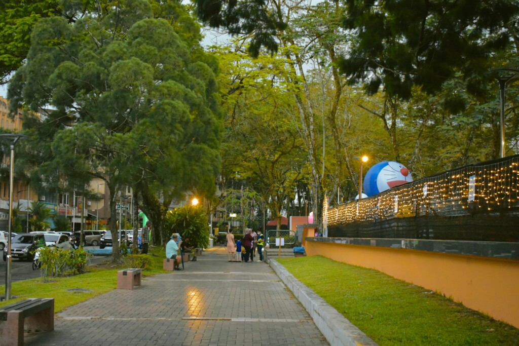 A peaceful park pathway with trees, fairy lights, and a large cartoon balloon.