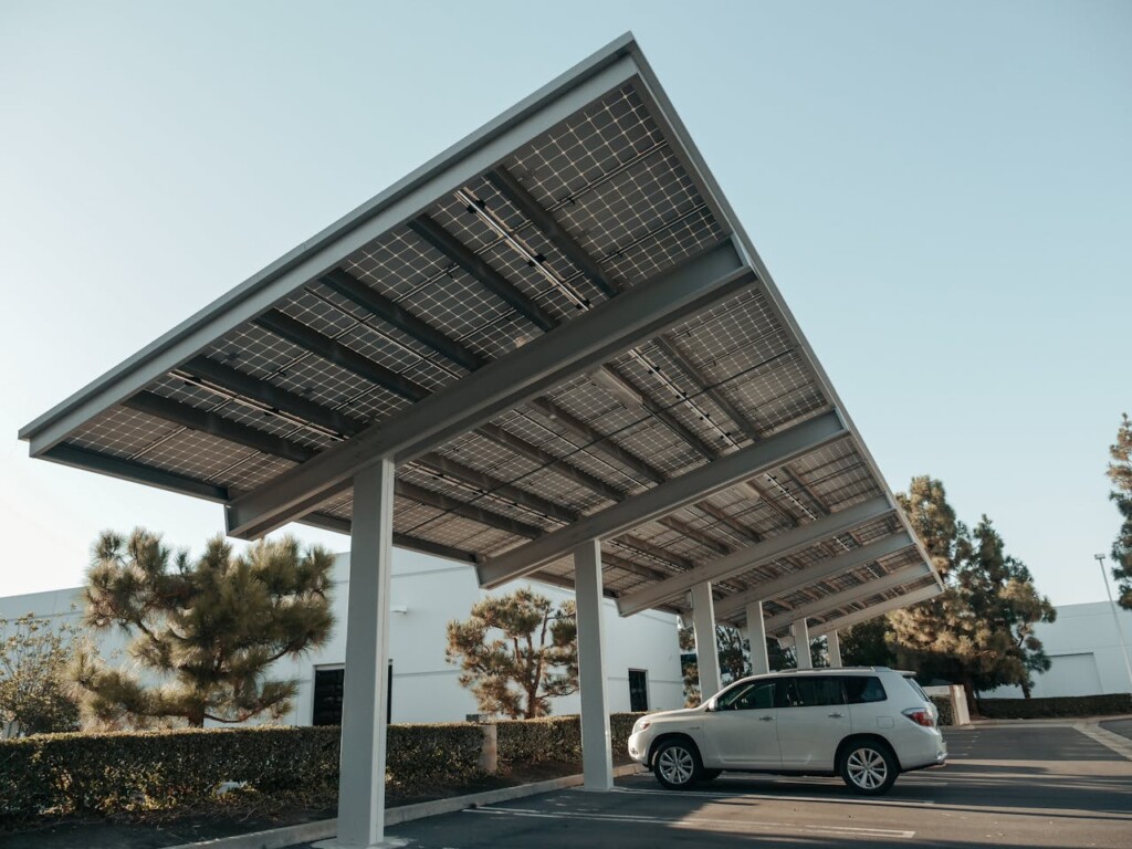 A white SUV parked under a solar panel carport in a parking lot.