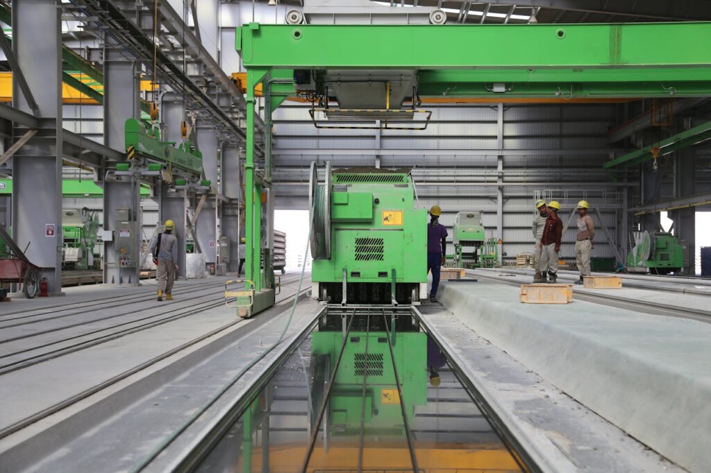 Workers operate machinery in a large, industrial factory with green equipment.