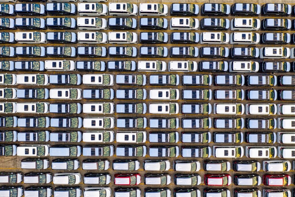 Aerial view of neatly parked white and black cars in rows.