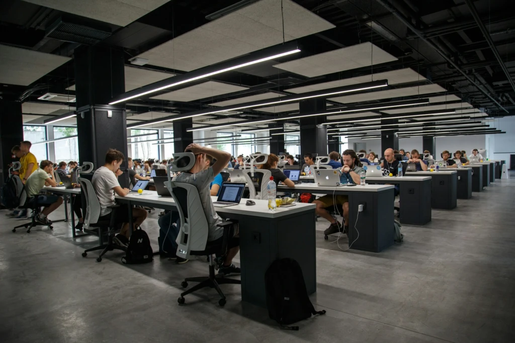 A large, modern office space with rows of people working on laptops.