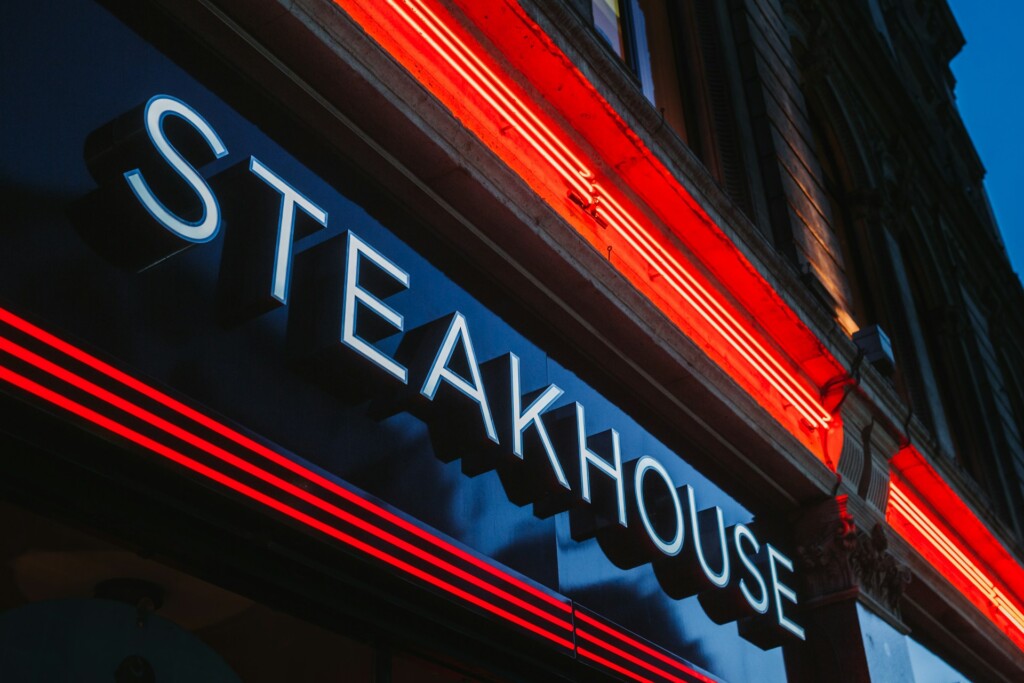 Illuminated steakhouse sign with red neon accents against a dark building.