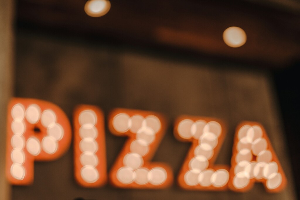 Blurred sign spelling "PIZZA" with glowing round lights in a dark setting.