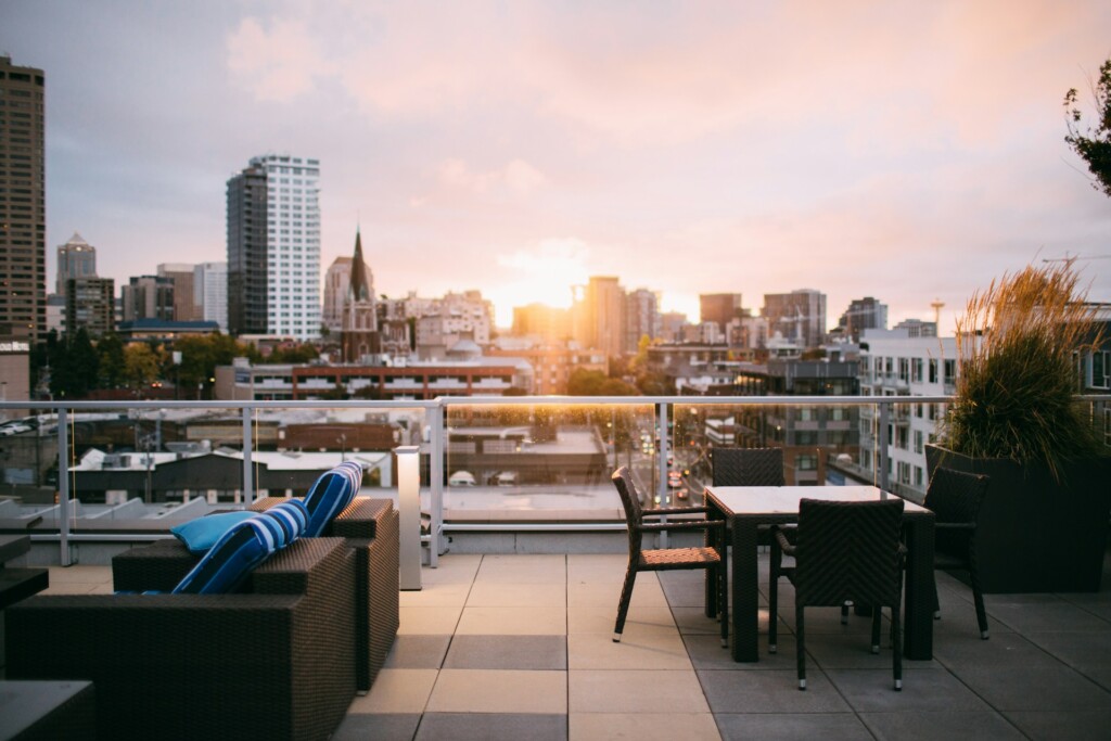 Rooftop patio with furniture overlooking a city skyline at sunset.