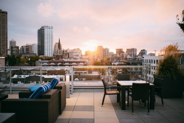 Rooftop patio with wicker furniture overlooking a city skyline at sunset.