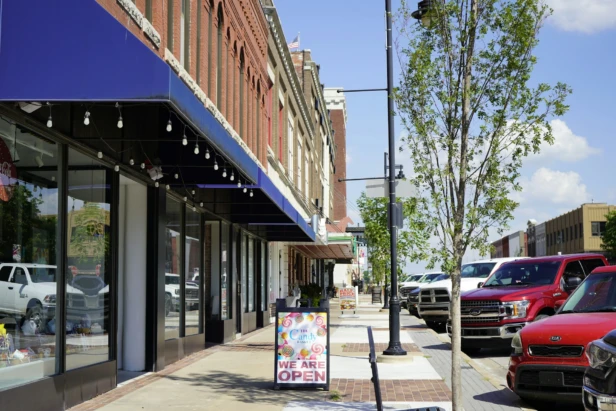 A downtown street scene with shops, parked cars, and a "We Are Open" sign.