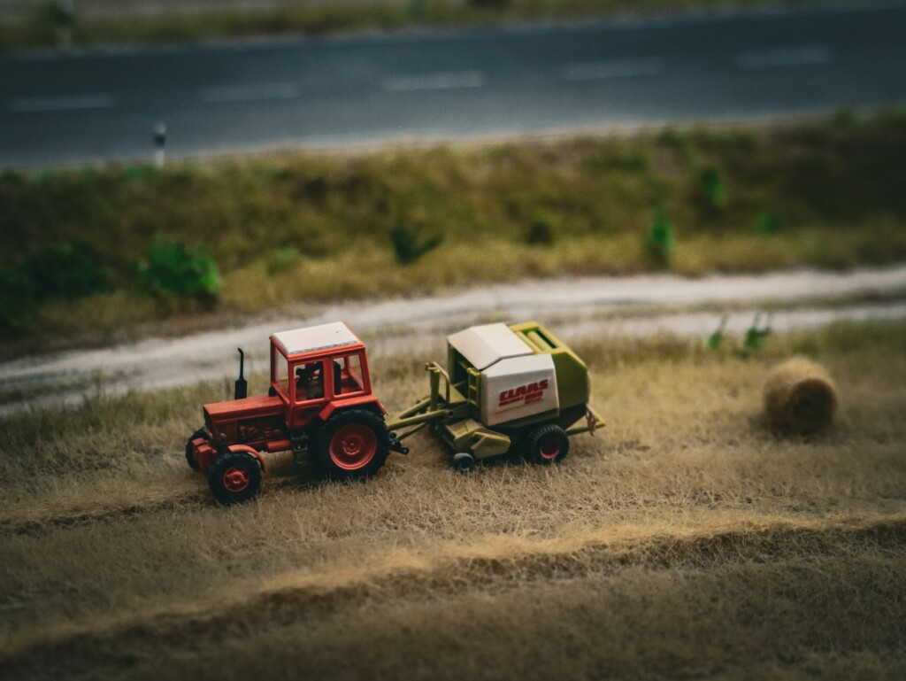 A miniature red tractor pulling a baler beside a country road.