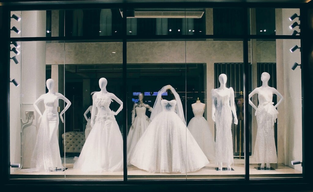 Mannequins in a store display showcase an array of elegant white wedding dresses.