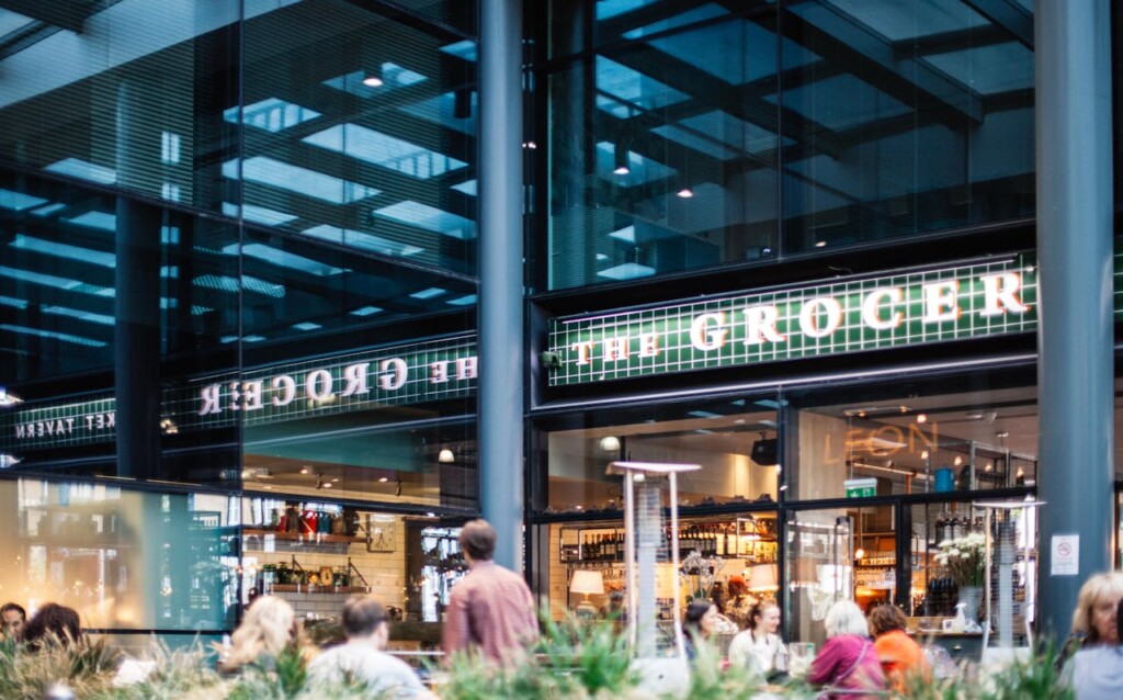 People sit outside a modern grocery store with a glass façade.