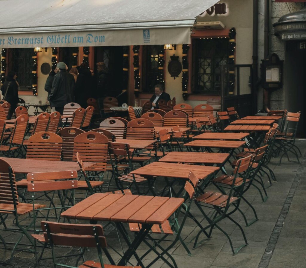 Outdoor seating with wooden tables and chairs outside a café in a city.