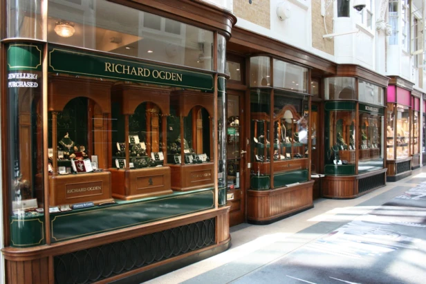 Elegant jewelry store facade with wooden displays and glass windows in a shopping arcade.