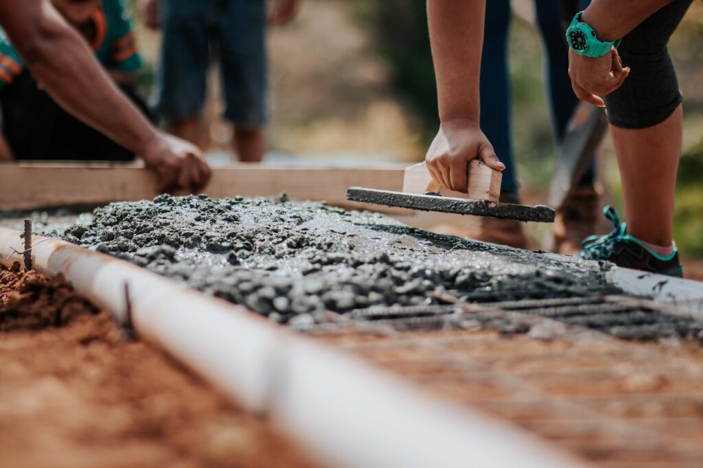 Workers smoothing wet concrete with a trowel on a construction site.