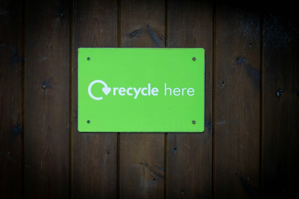 A green "recycle here" sign on a wooden wall.