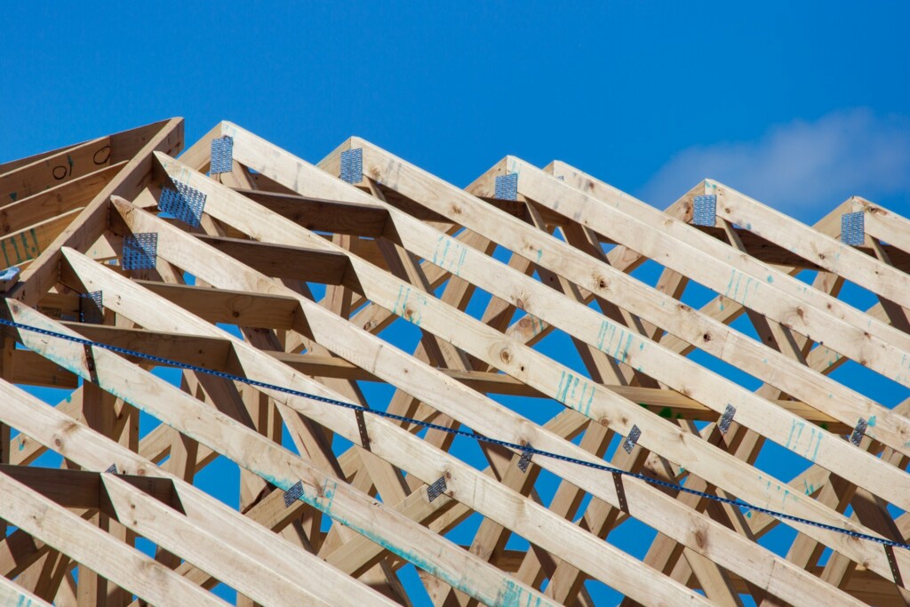 Wooden roof trusses against a clear blue sky on a sunny day.