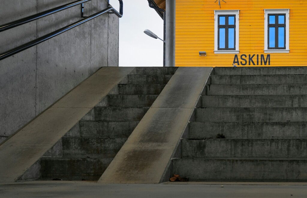 Concrete stairs and ramp leading to a bright yellow building with windows.