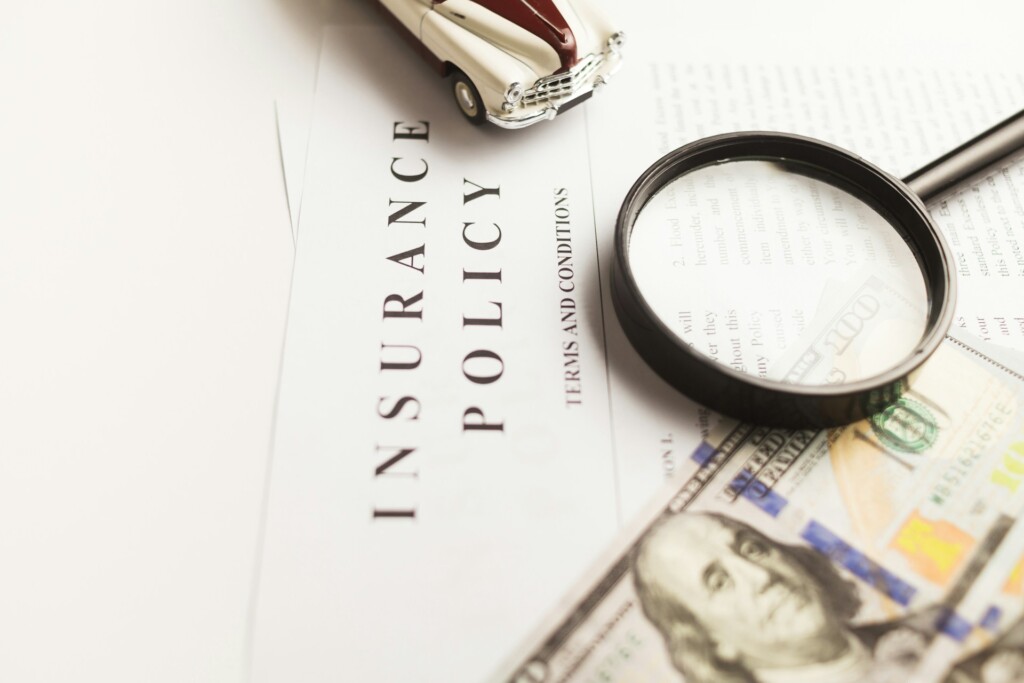 A magnifying glass, toy car, and US dollar bill on an insurance policy.