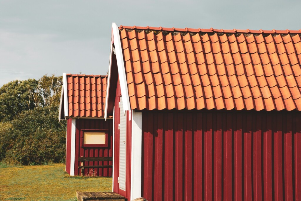 Two red wooden cabins with orange tiled roofs in a grassy area.
