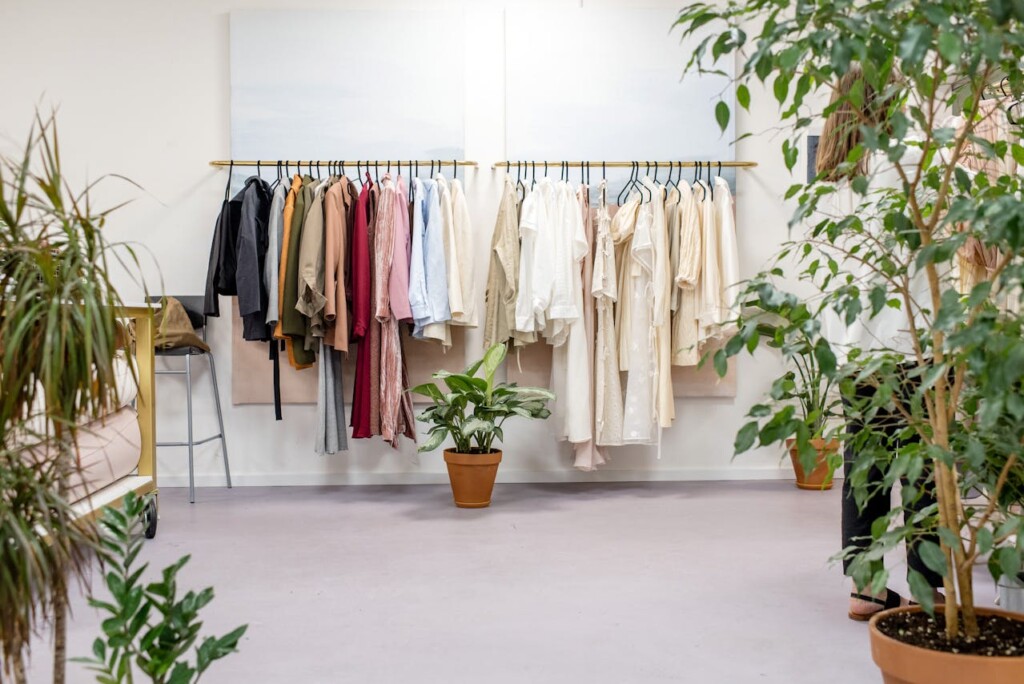 Clothing rack in a boutique surrounded by green indoor plants.