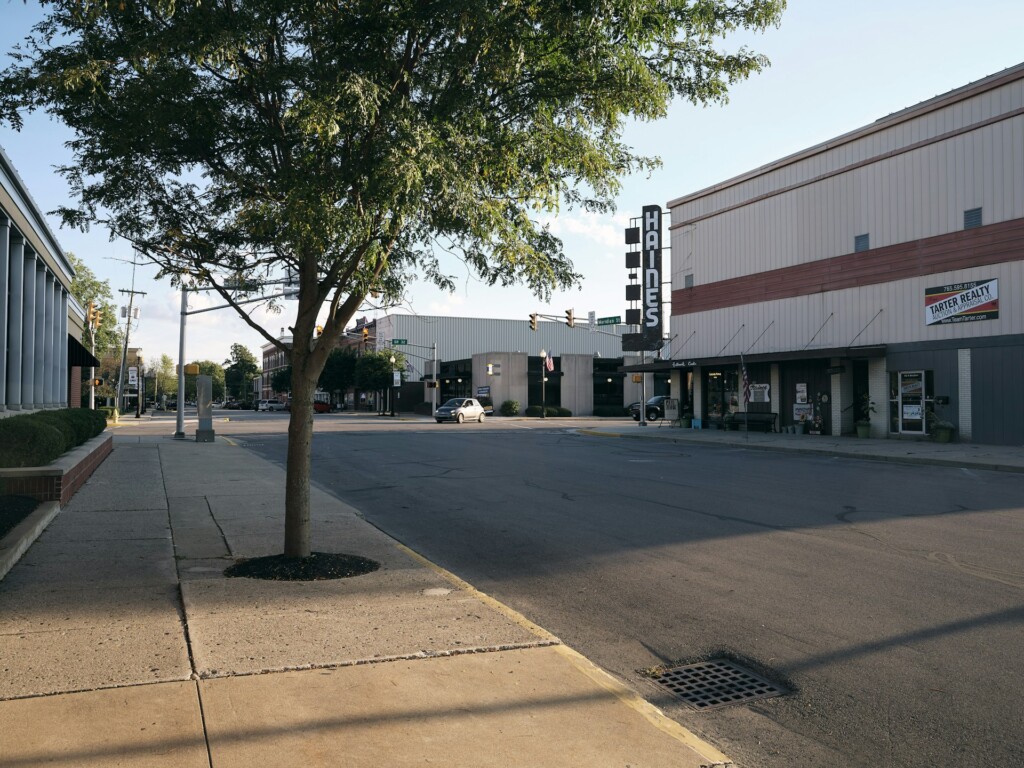 Empty street in small town with tree, storefronts, and vintage theater sign.