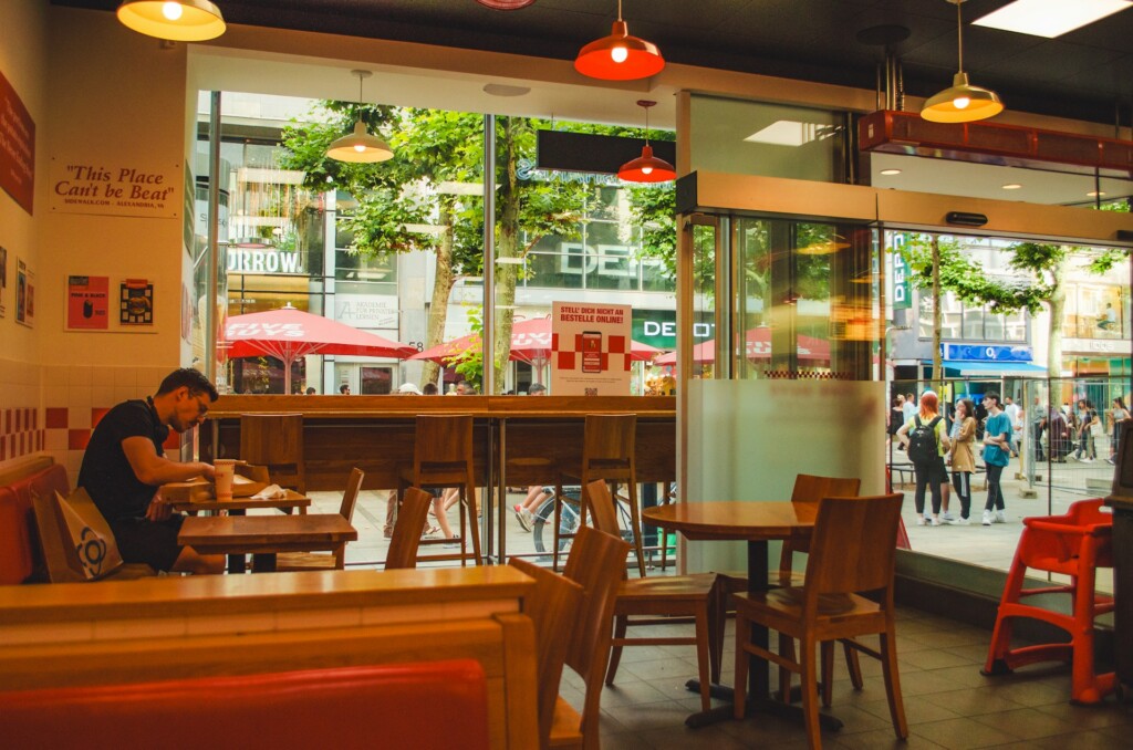 A man sits alone in a fast-food restaurant near a large window.