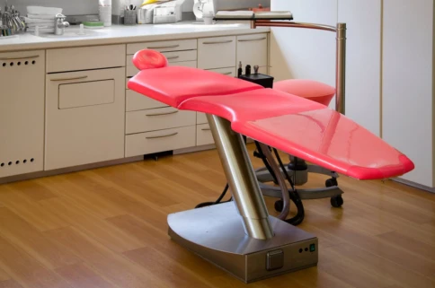 A modern red dental chair in a clean, well-equipped clinic room.