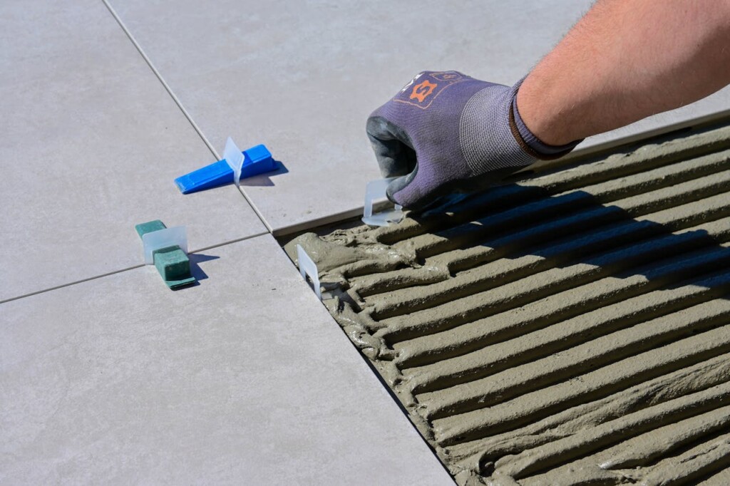 A person wearing gloves installs large floor tiles using a leveling system.